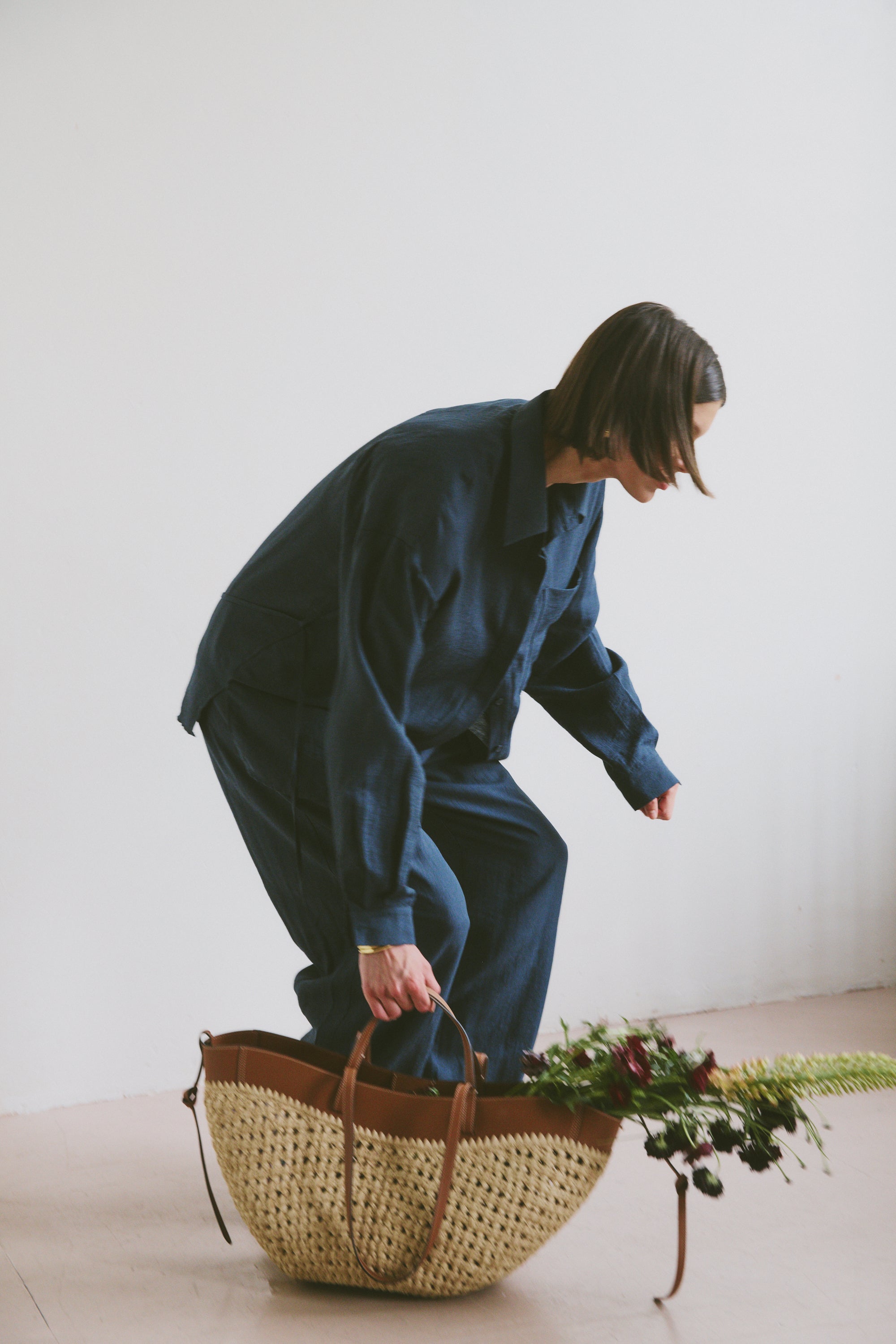 Model in blue outfit with a woven basket and flowers on a light background
