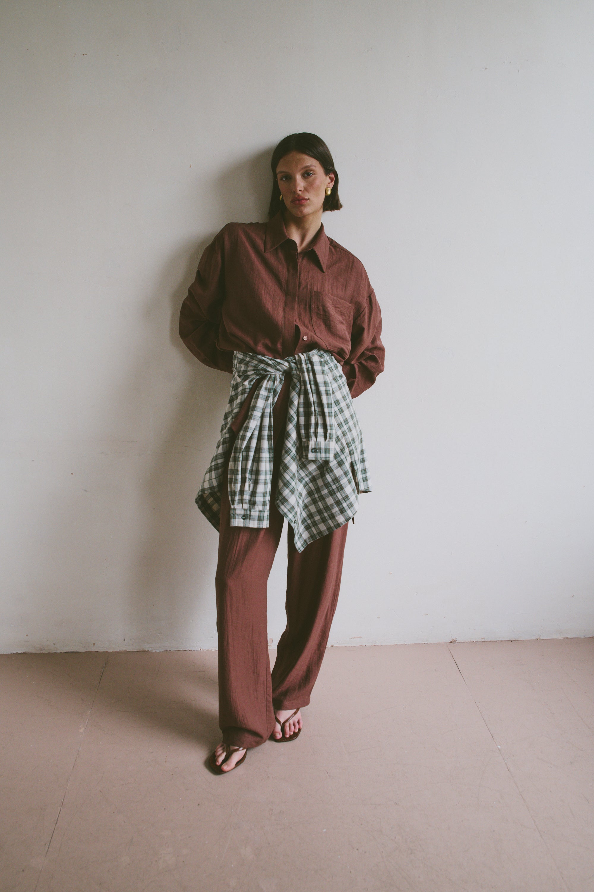 Model wearing a red shirt and plaid skirt against a white wall