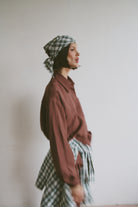Model wearing a maroon shirt with a plaid headscarf and matching shirt tied around the waist 