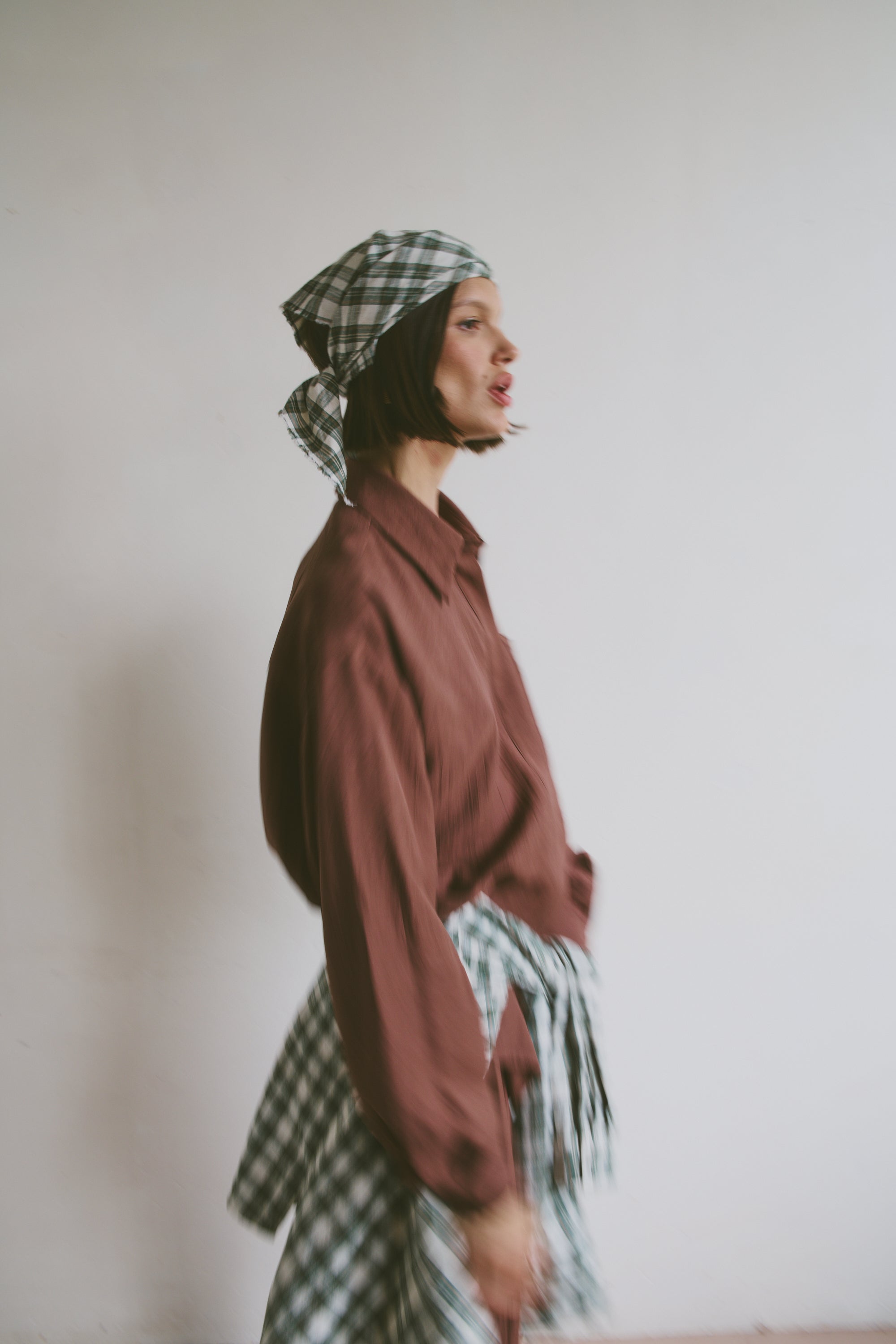 Model wearing a maroon shirt with a plaid headscarf and matching shirt tied around the waist 