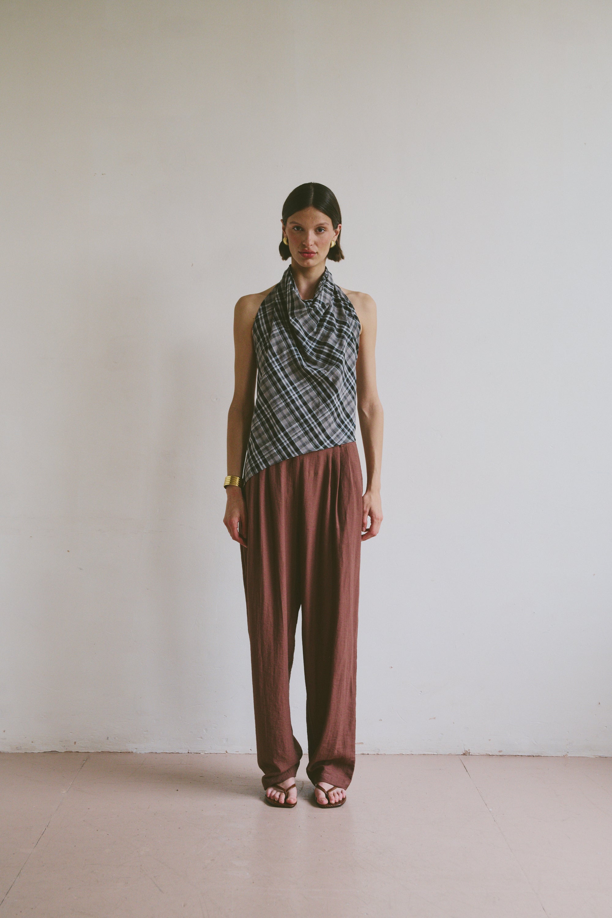 Model wearing a patterned top tied at the neck and maroon brown trousers against a plain background
