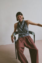 Woman laughing while sitting on a chair wearing a plaid top and burgundy pants against a plain background
