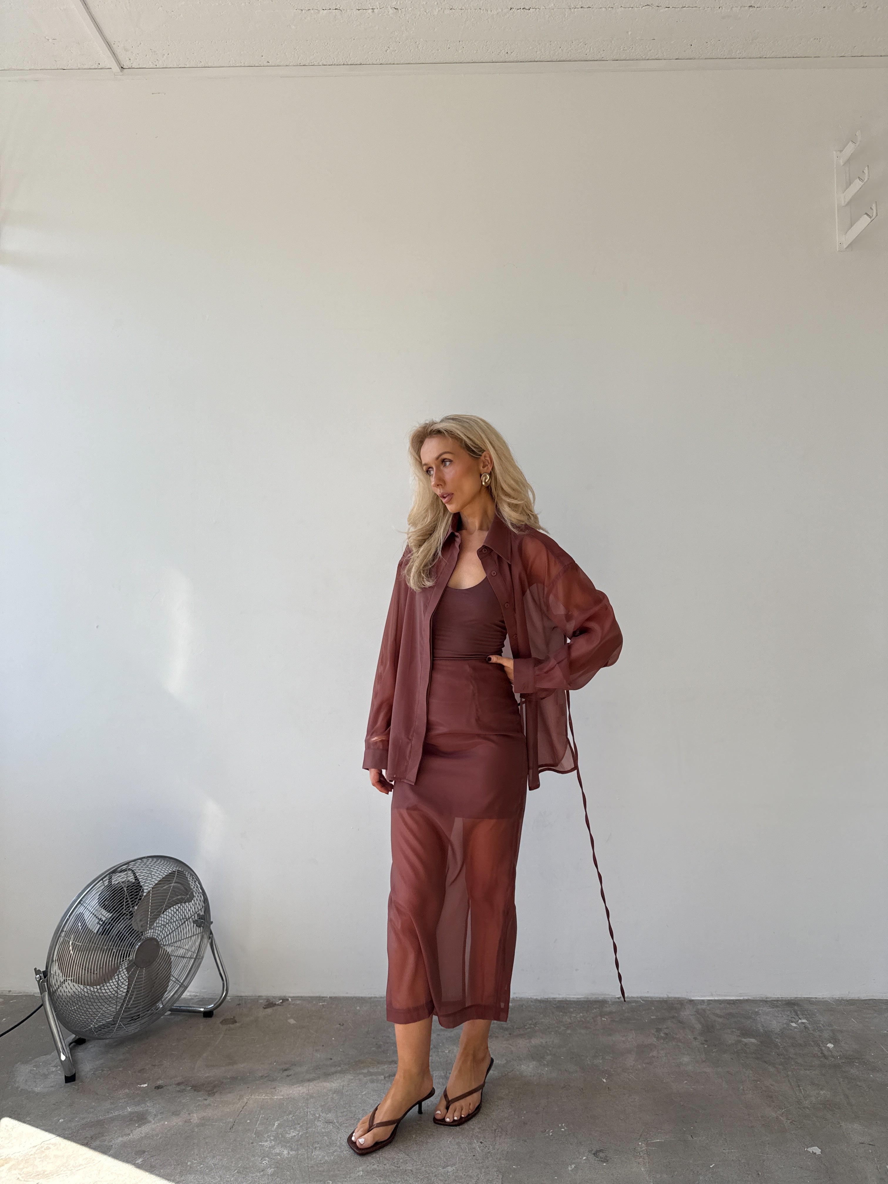 Model wearing a deep red semi-sheer shirt with matching vest and skirt with black sandals