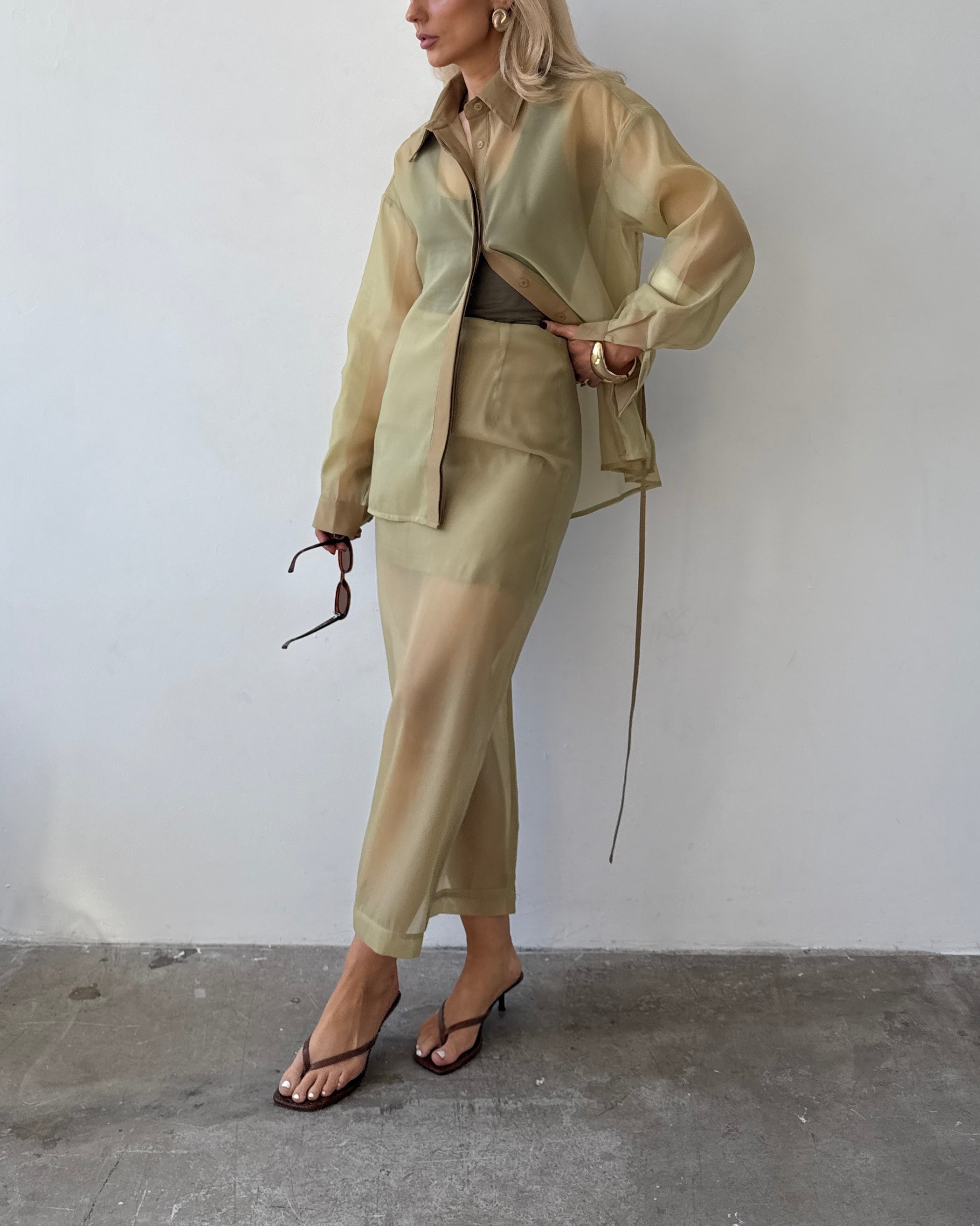 Model wearing a semi-sheer pale olive shirt over a olive fitted vest with matching semi-sheer skirt