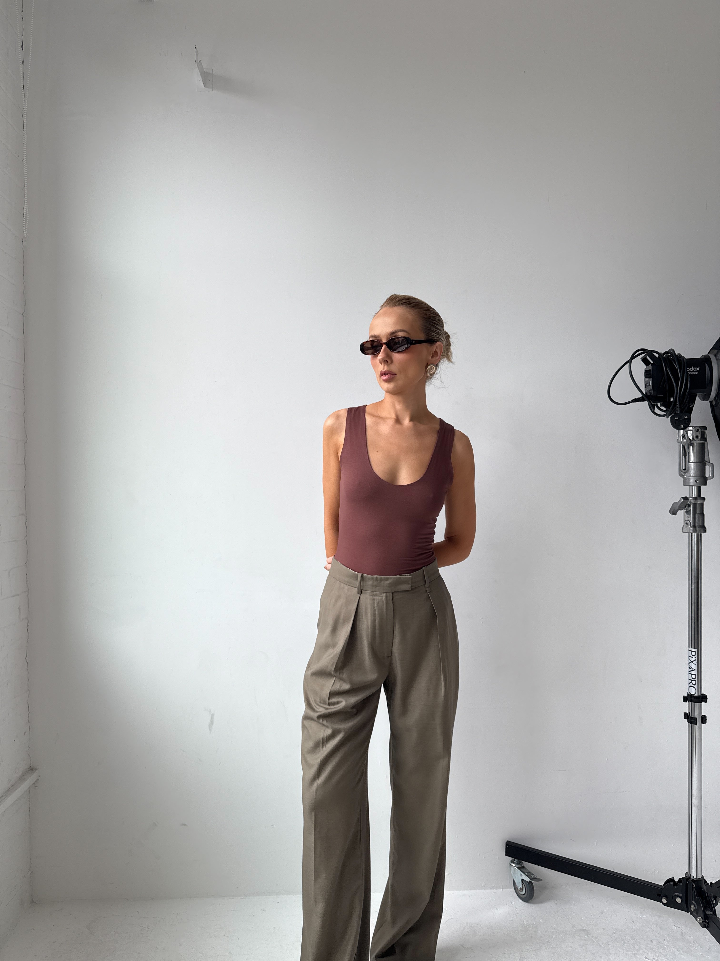 Model wearing a brown tank top, beige trousers and sunglasses in a studio setting with camera equipment