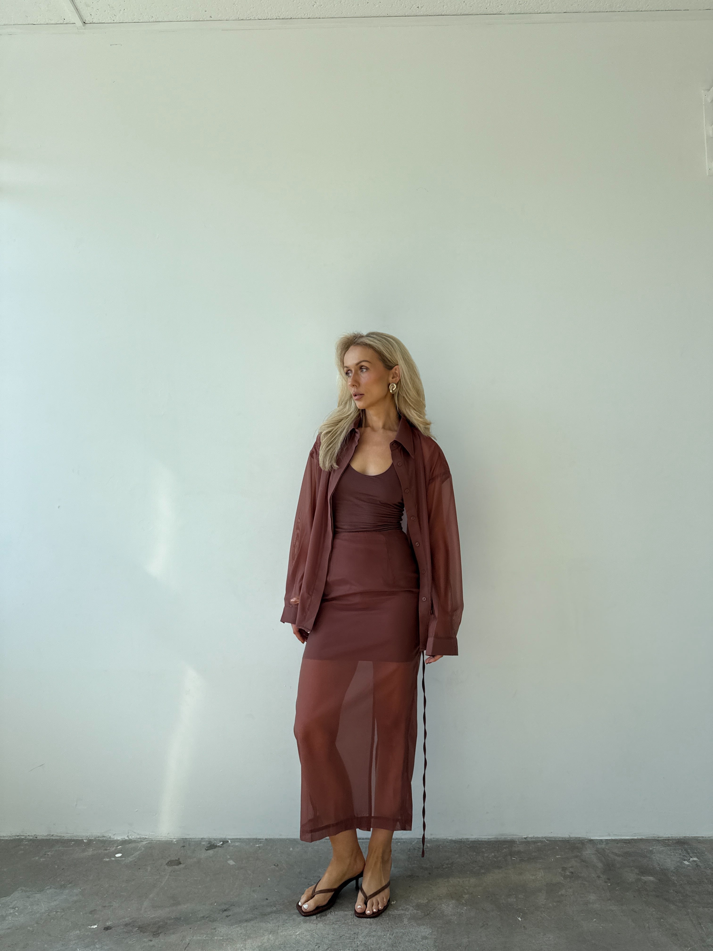 Model wearing a maroon outfit standing against a white wall