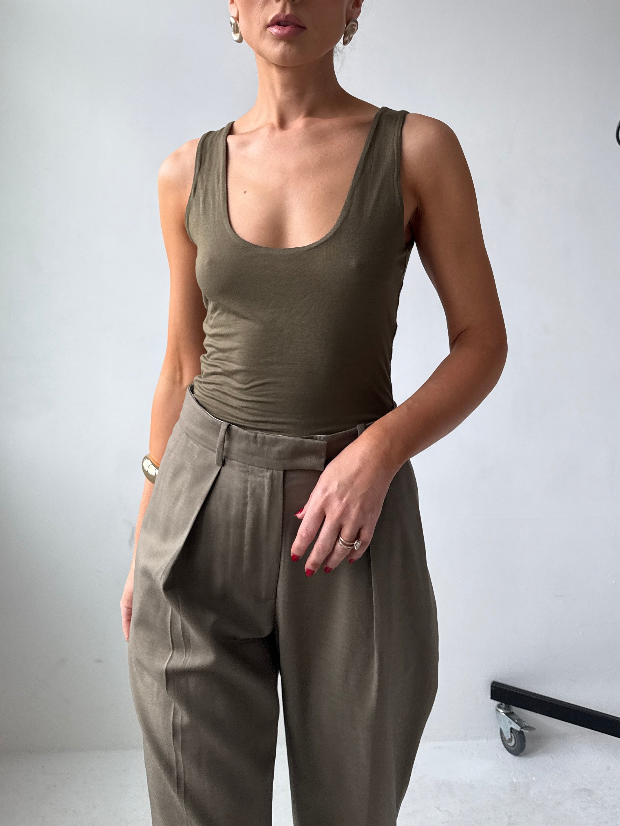 Model wearing a fitted olive green tank top and high-waisted pants against a plain background