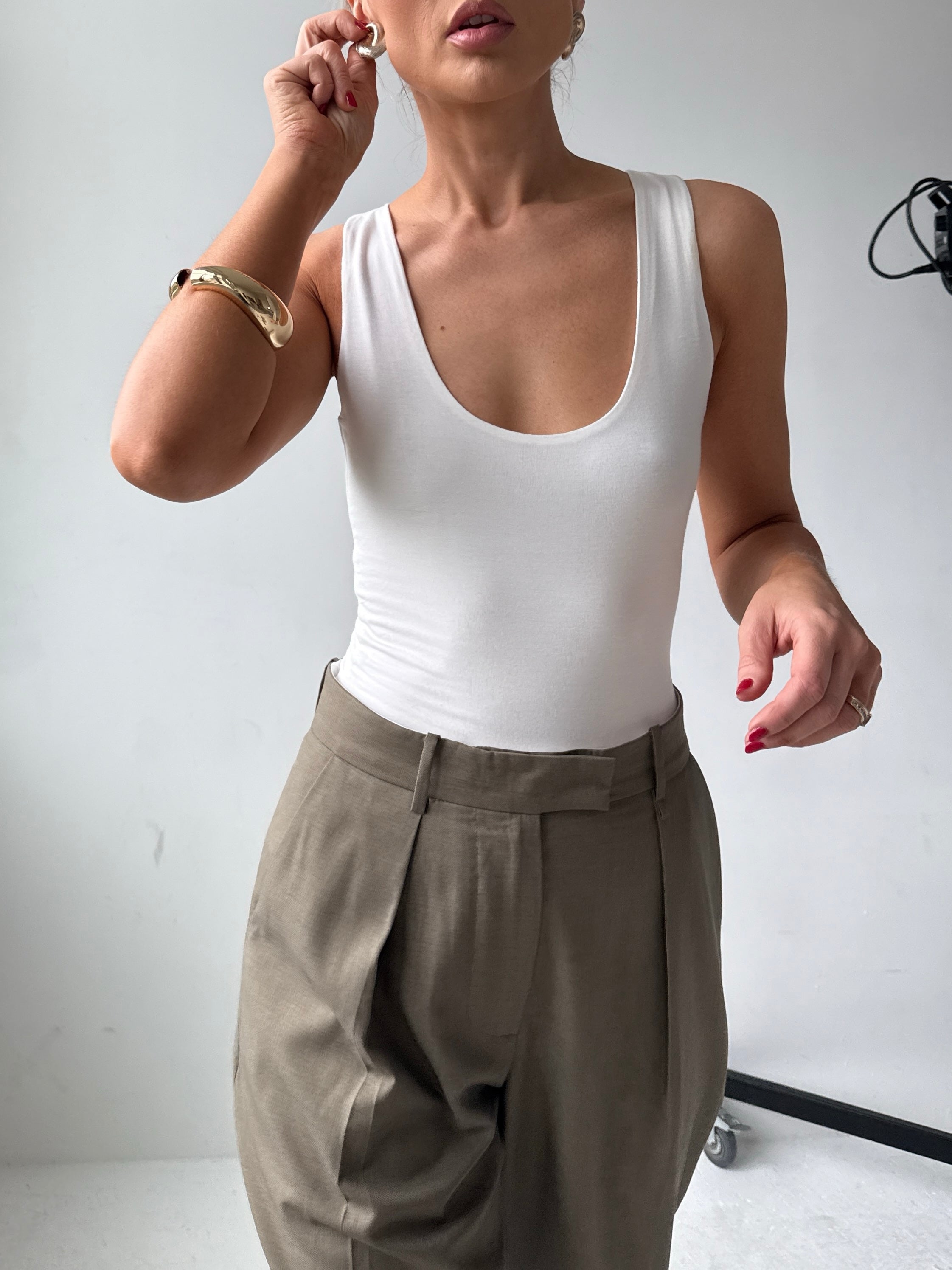 Model wears a fitted white scoop neck tank top with tailored trousers and gold jewellery 