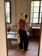 Model taking a mirror selfie wearing a brown top and black pants in a room with large windows