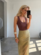 Woman taking a mirror selfie wearing a brown top and a yellow skirt in a minimalistic room