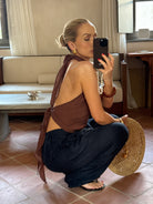 Person taking a mirror selfie crouching, while wearing a brown top and black trousers