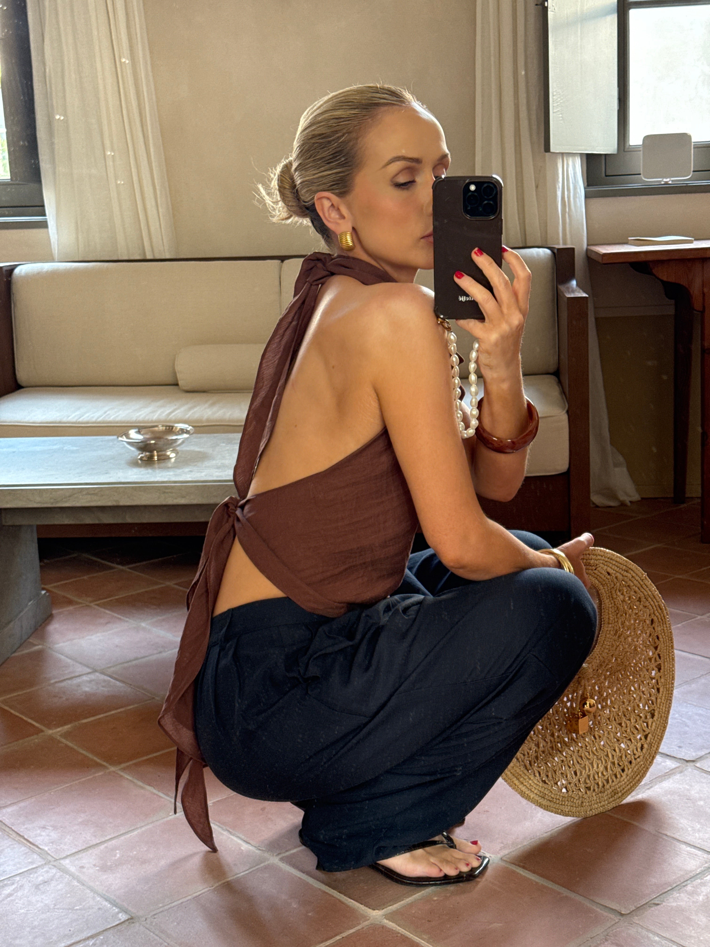 Person taking a mirror selfie crouching, while wearing a brown top and black trousers
