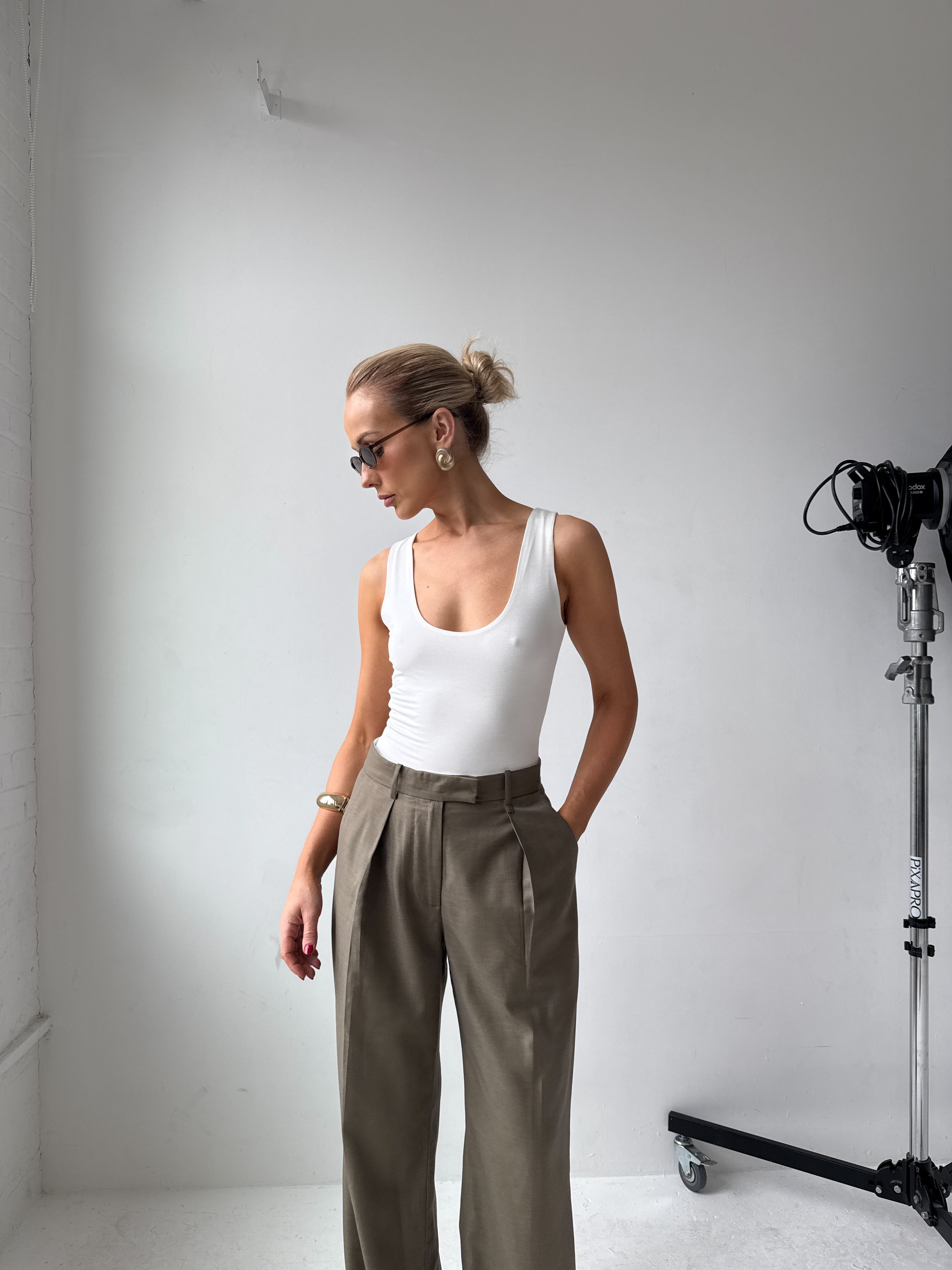 Model in a white tank top and grey trousers standing in a studio setting