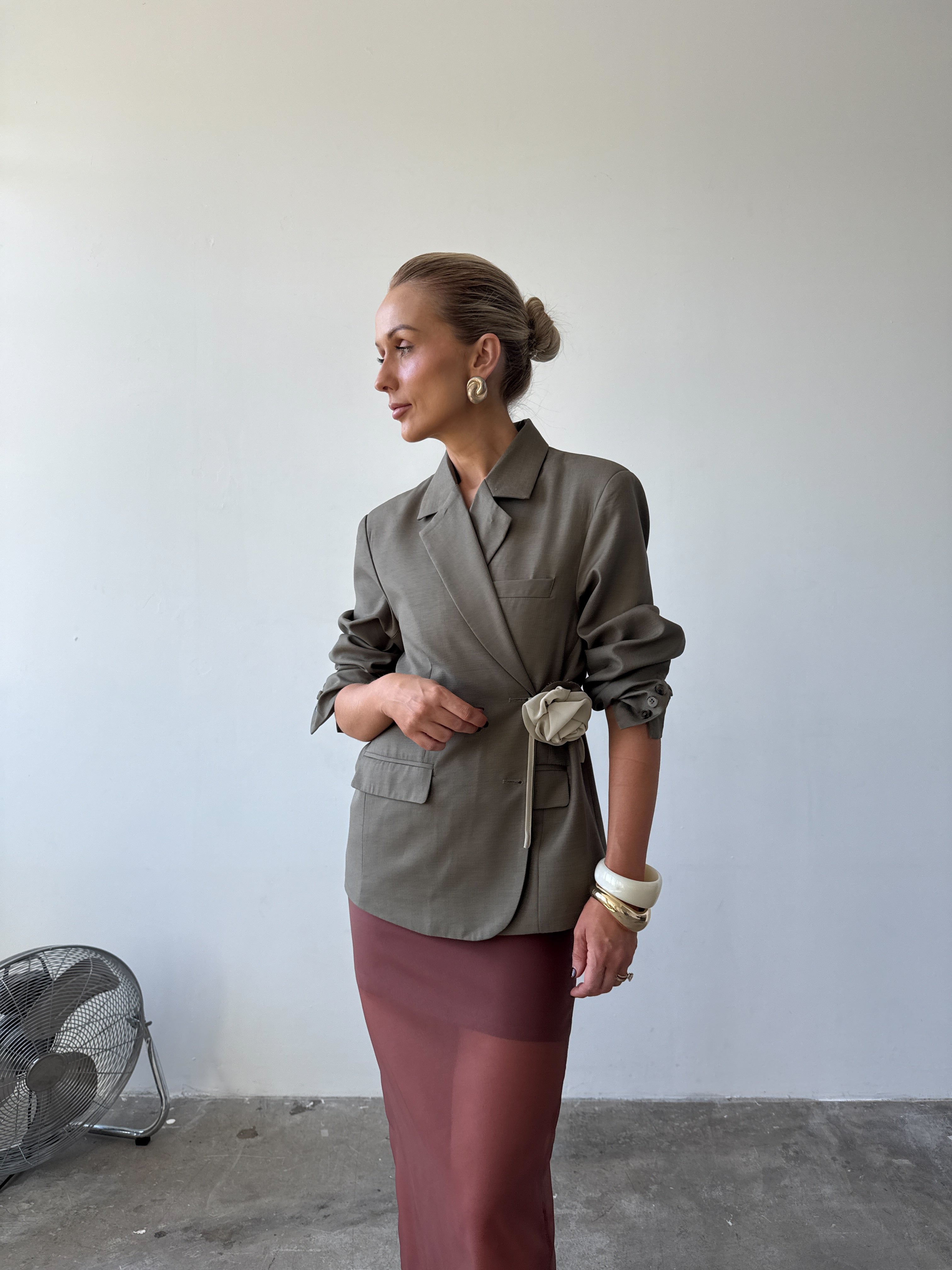 Model is wearing the olive Margaux blazer styled in a wrap-over look with pushed up sleeves paired with the Romée Skirt in Sienna