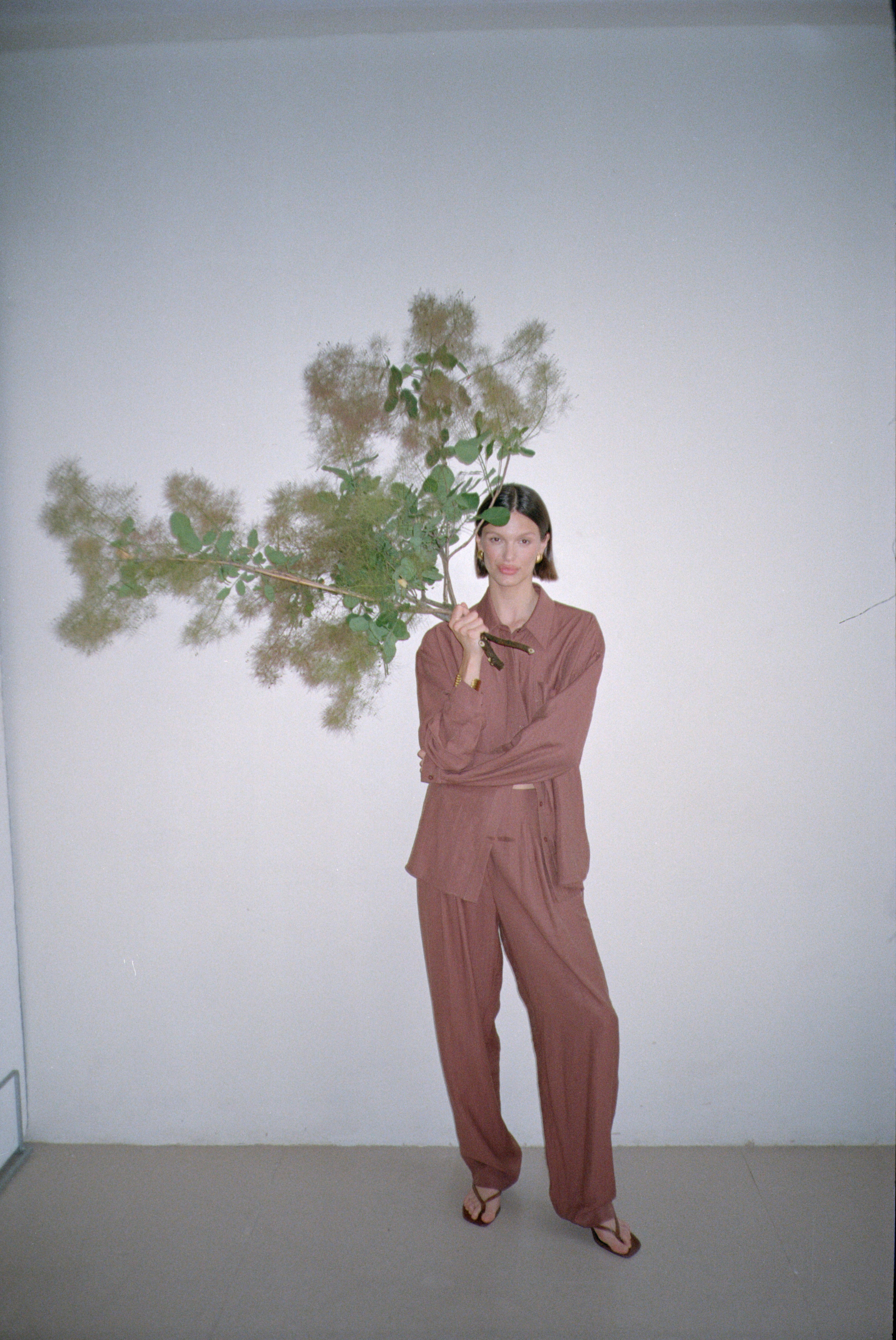 Model wearing a brown outfit standing with large decorative branches in their grasp