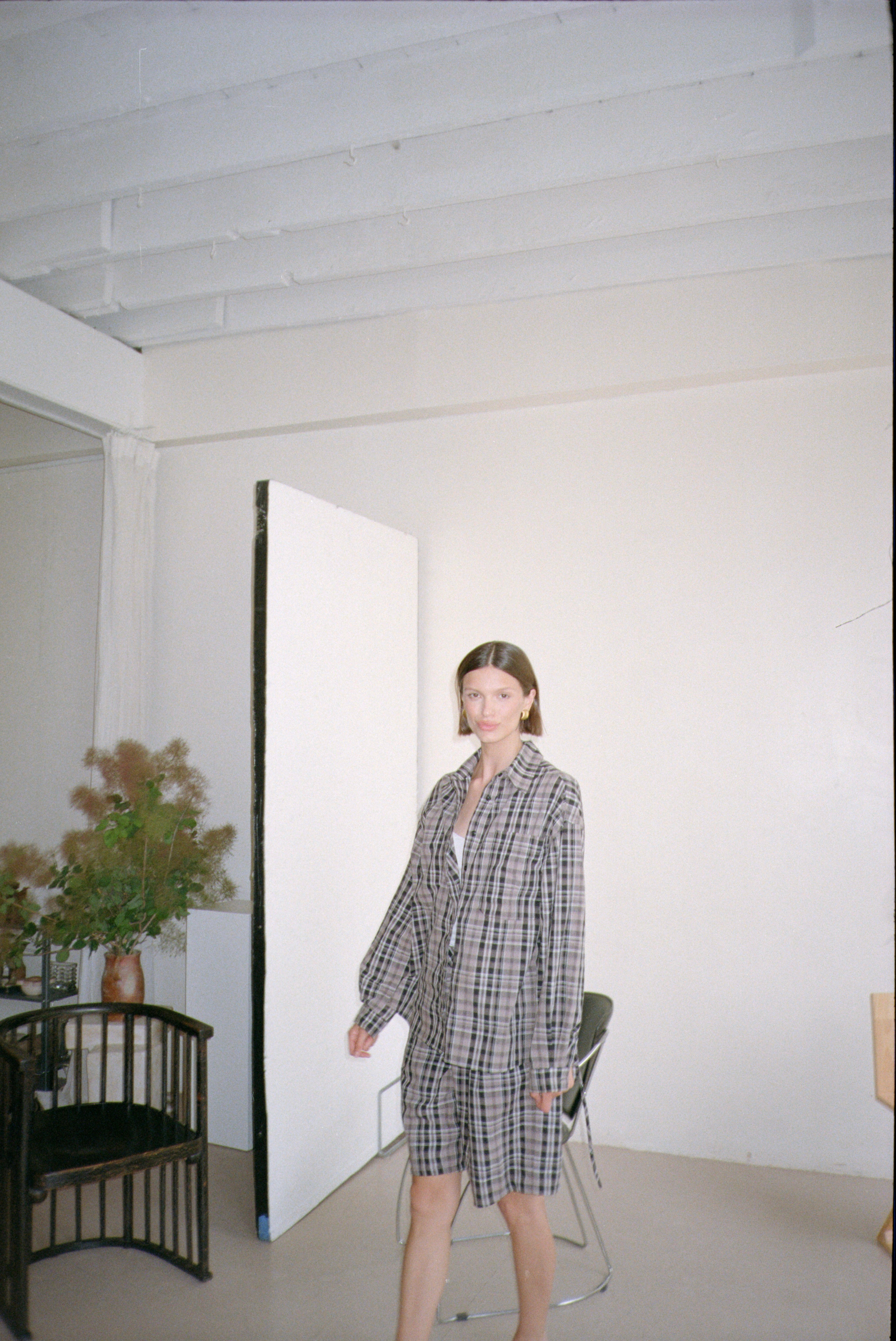 Woman in a checkered outfit standing in a minimalistic room with white walls