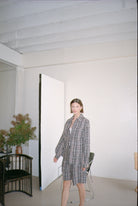 Woman in a checkered outfit standing in a minimalistic room with white walls