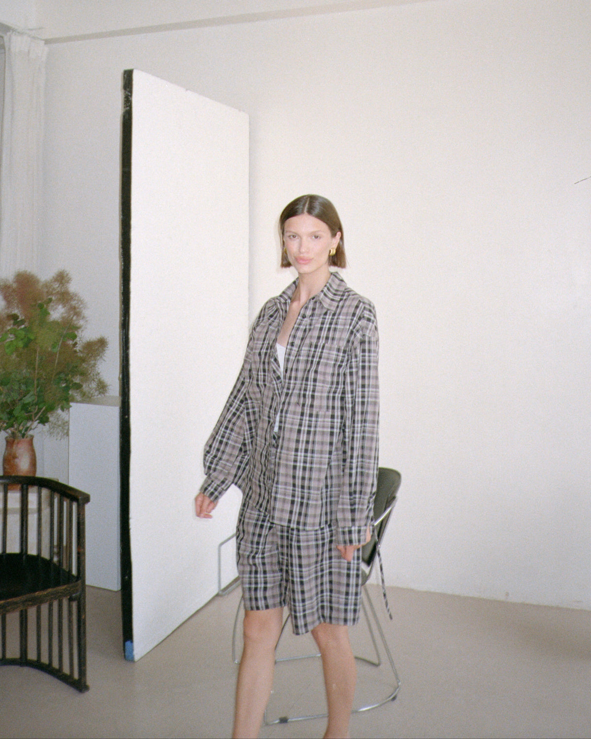 Woman in a checkered outfit standing in a minimalistic room with white walls