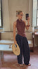 Model taking a mirror selfie while wearing a brown top and flowy navy trousers while holding a woven bag